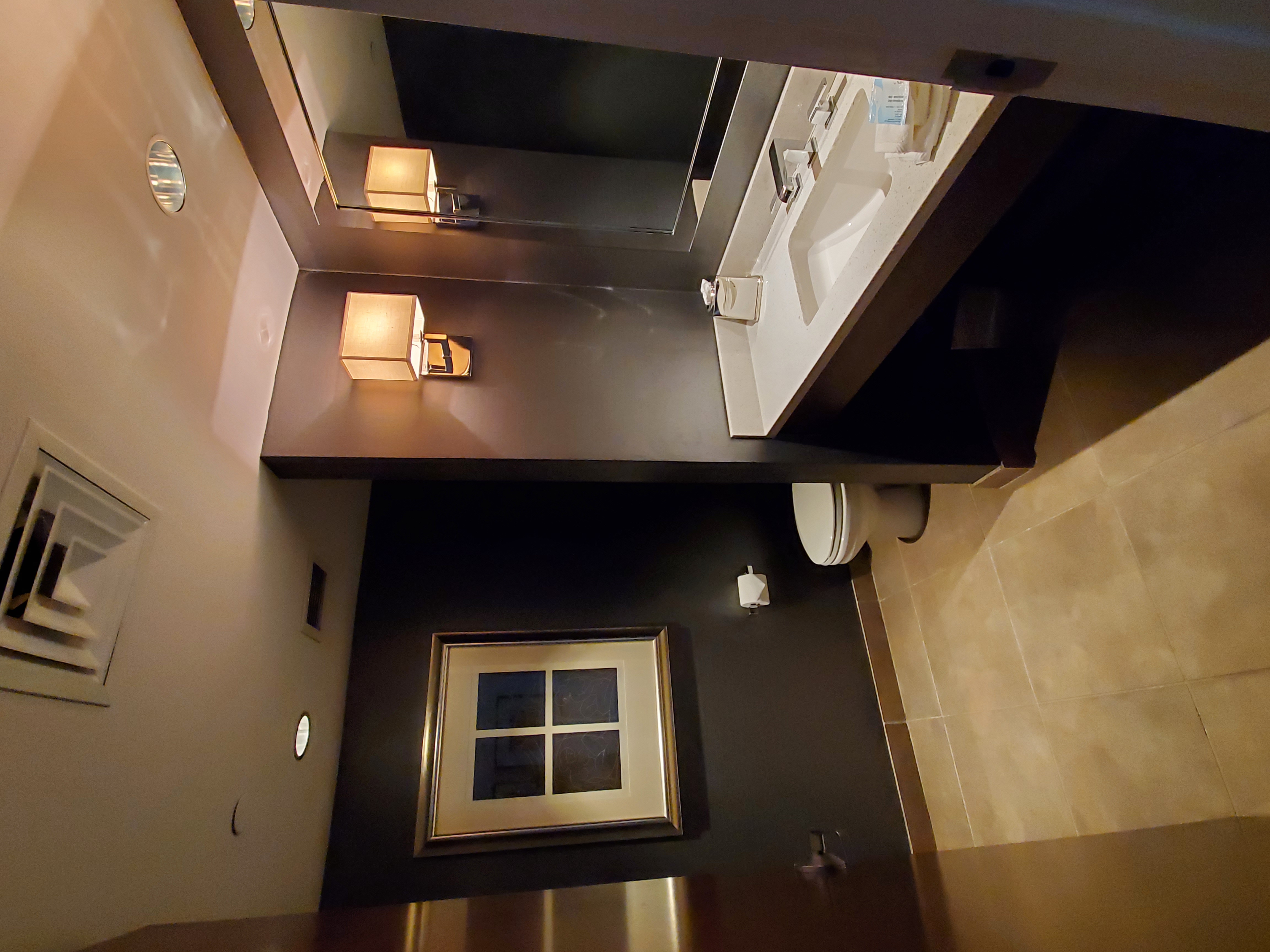 A clean and modern bathroom with a white sink, large mirror, and wall lights.