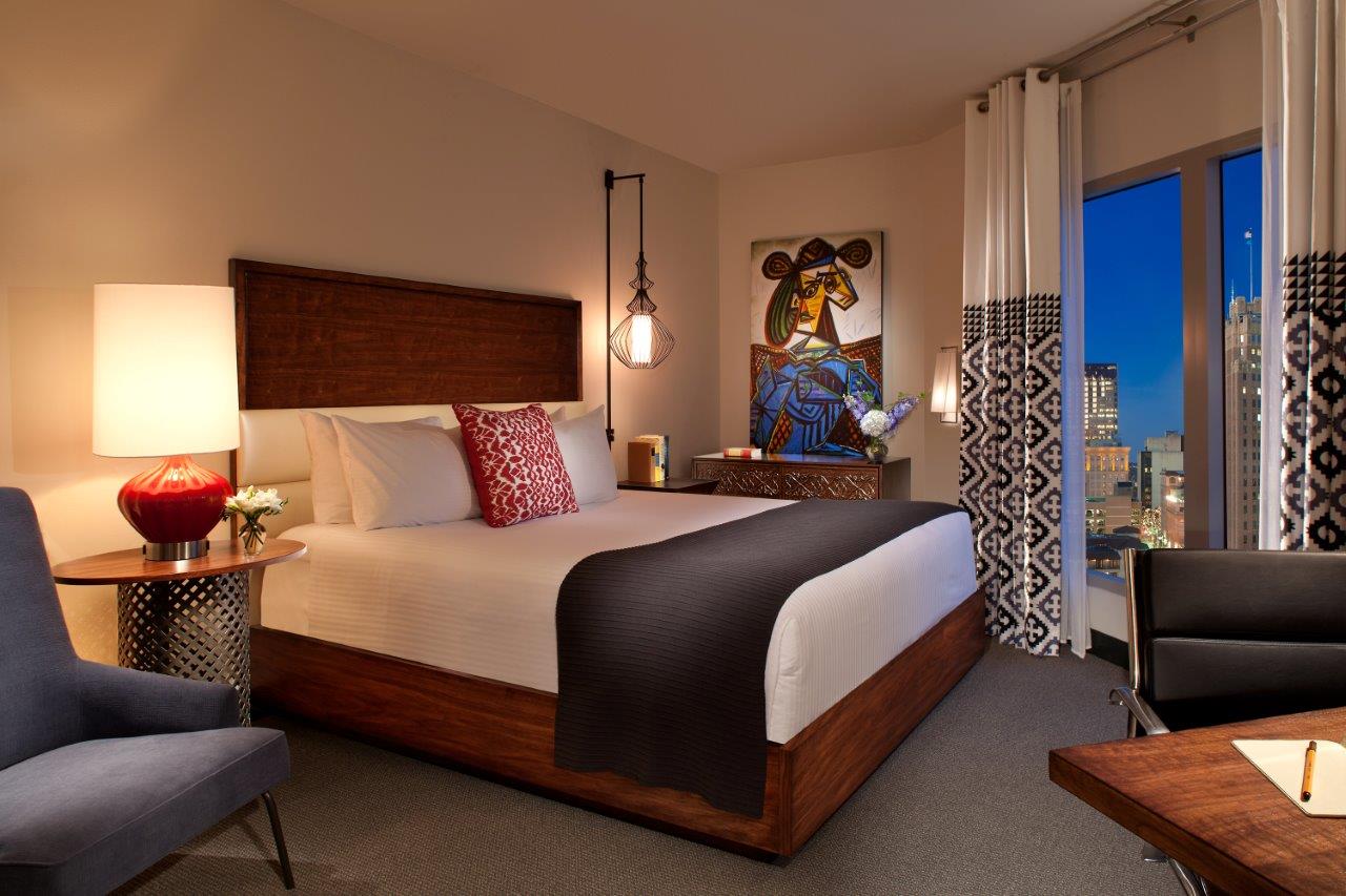 A hotel room with a king-sized bed, city view, and artwork.