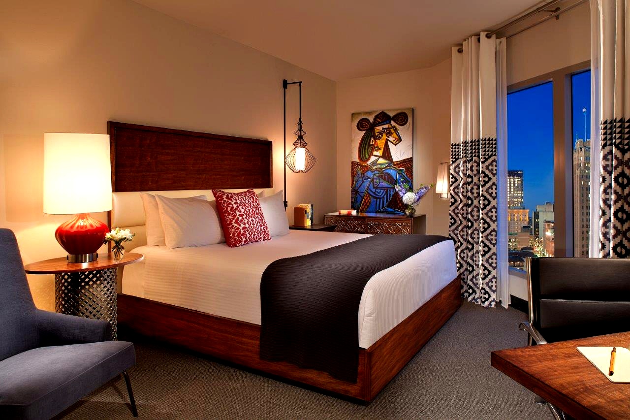 A hotel room with a large bed, artwork, and a lamp.