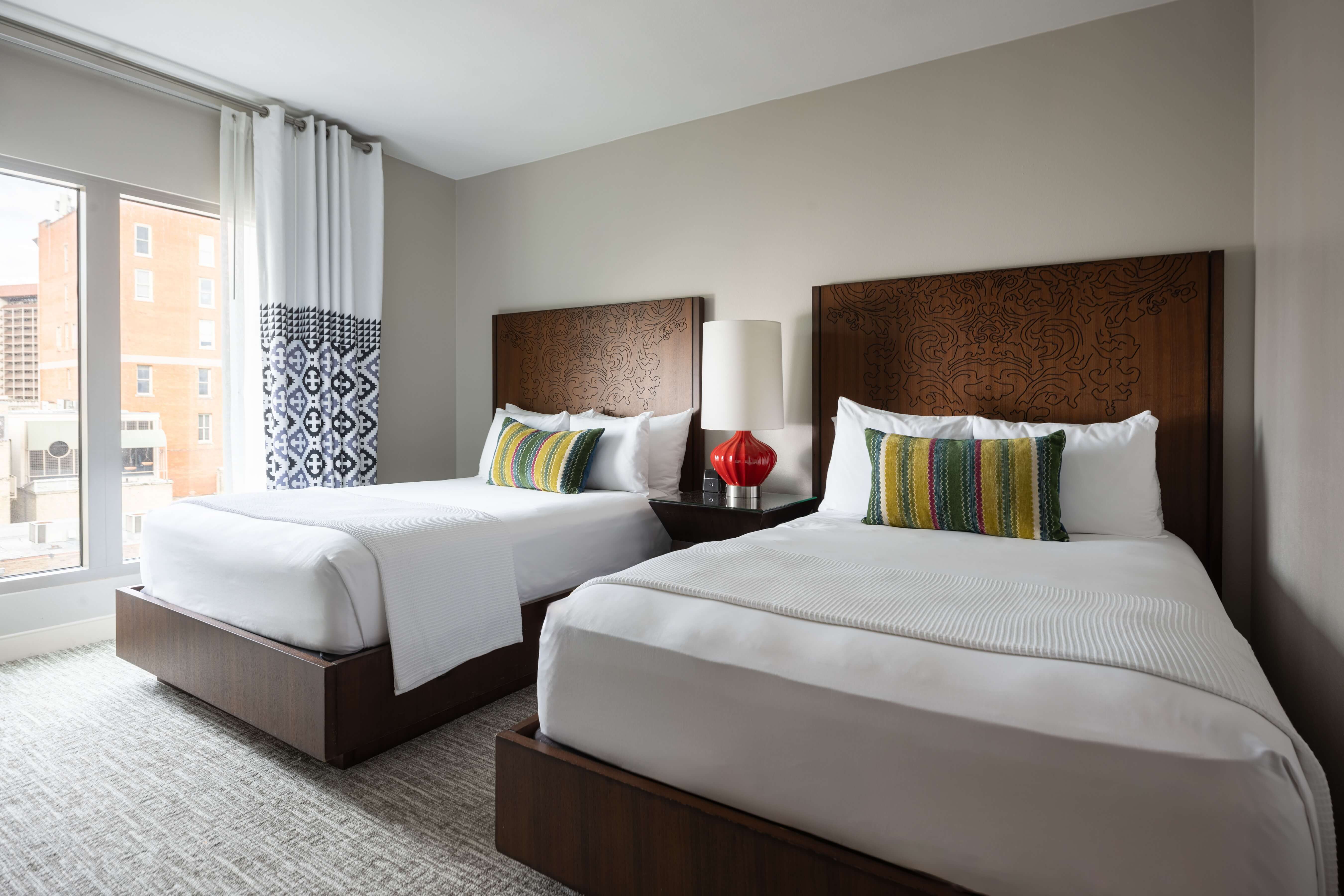 A hotel room with two twin beds, wooden headboards, and a city view.