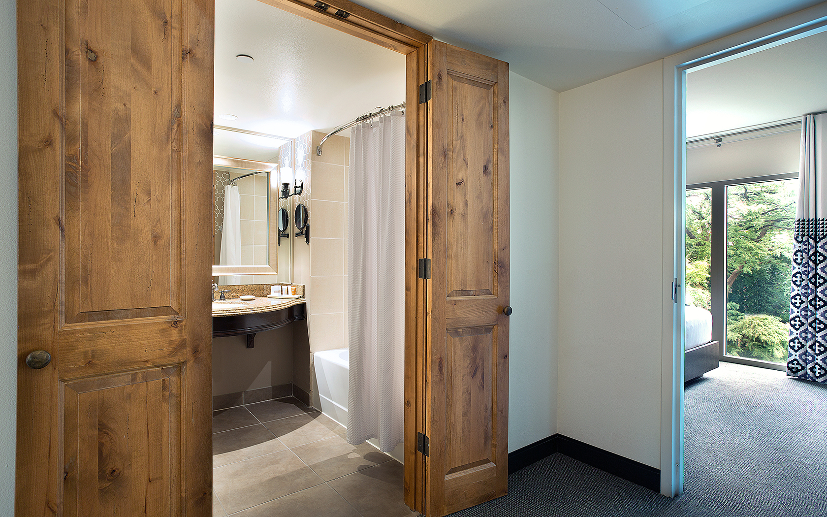 A bathroom interior with a bathtub, shower curtain, sink, and mirror, partially obscured by wooden doors.