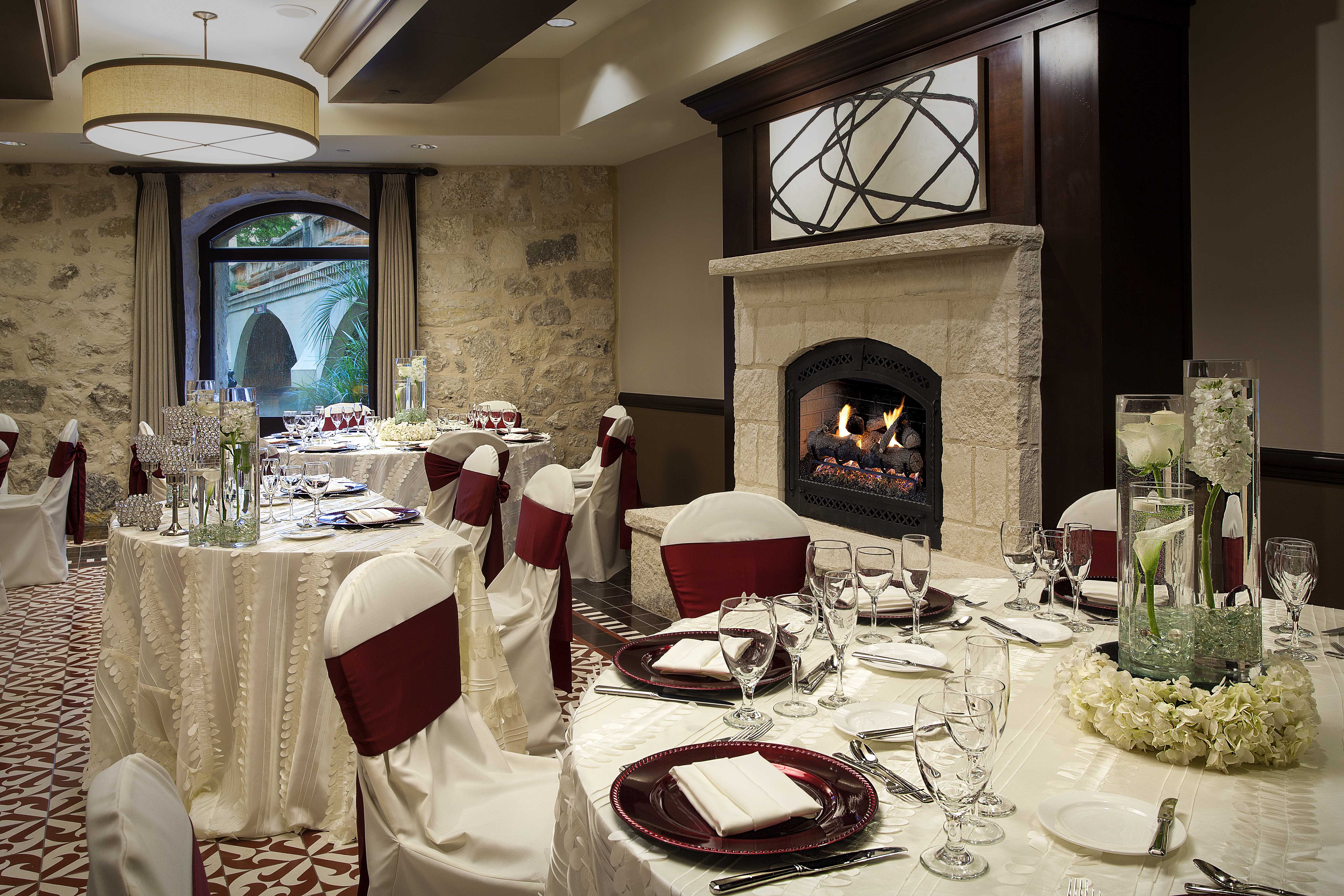 A formal dining area with a fireplace, stone walls, and arched windows.