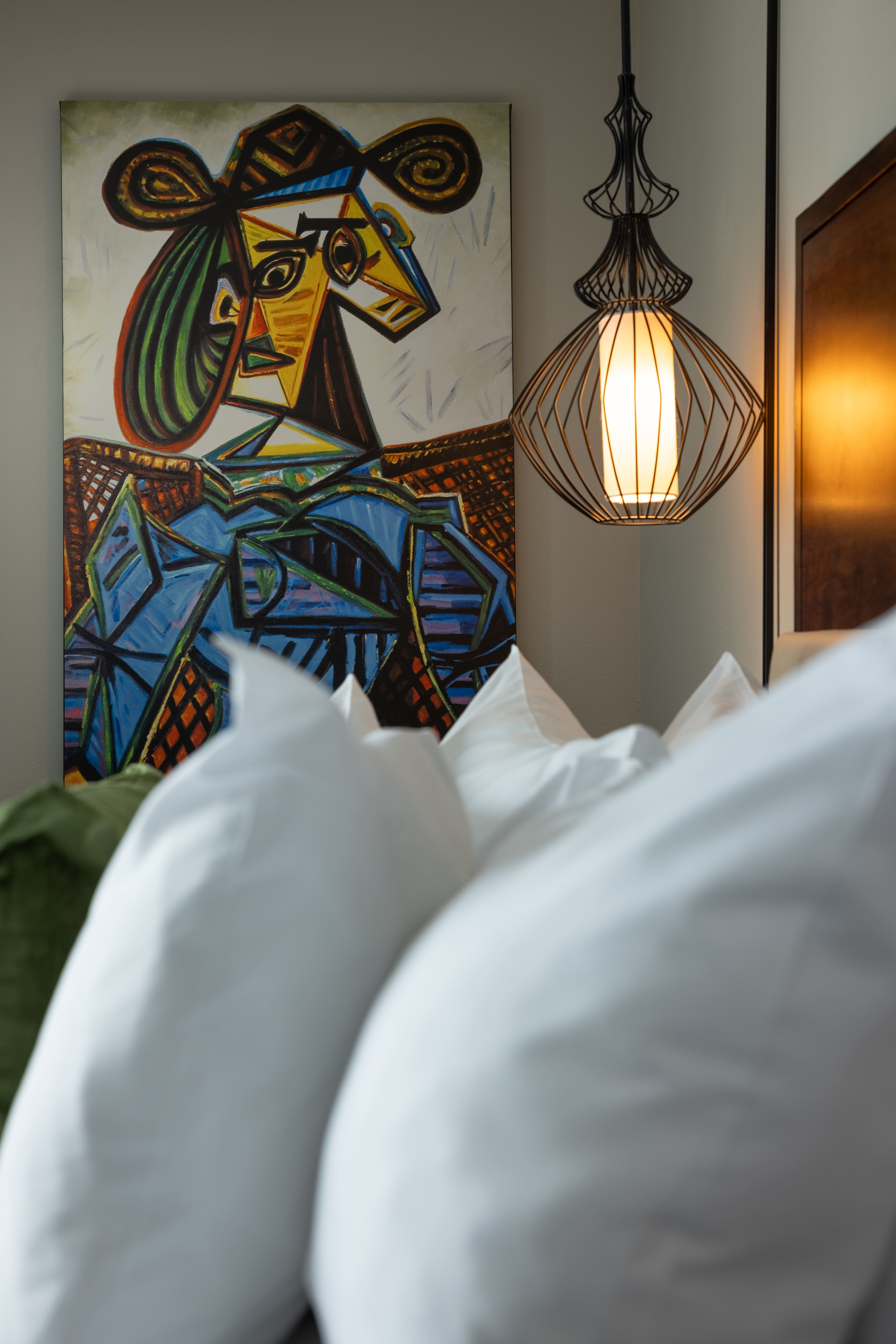 A close-up of a bed with white pillows and a colorful abstract artwork in the background.