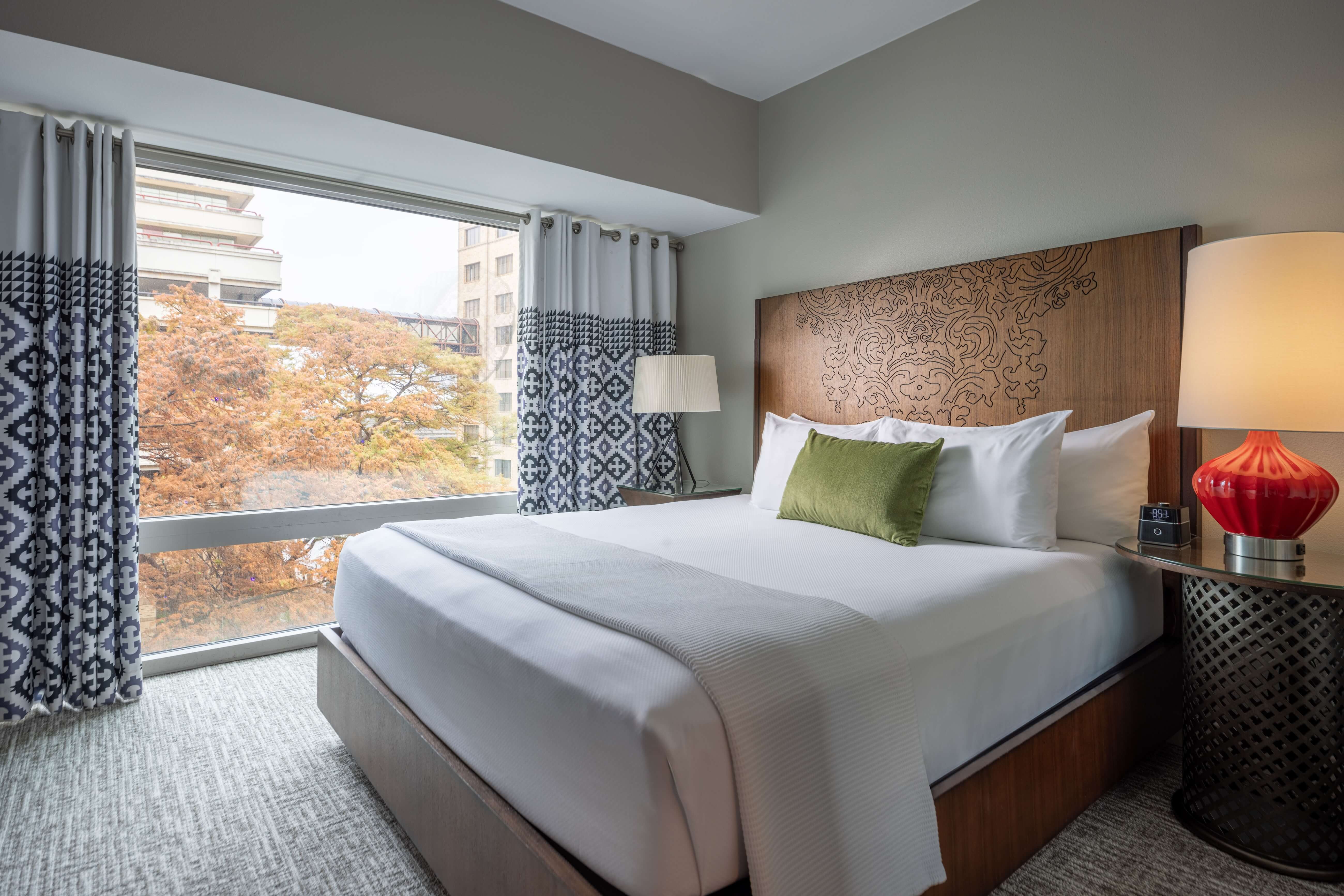 A hotel room with a large window, a wood headboard, and white bedding.