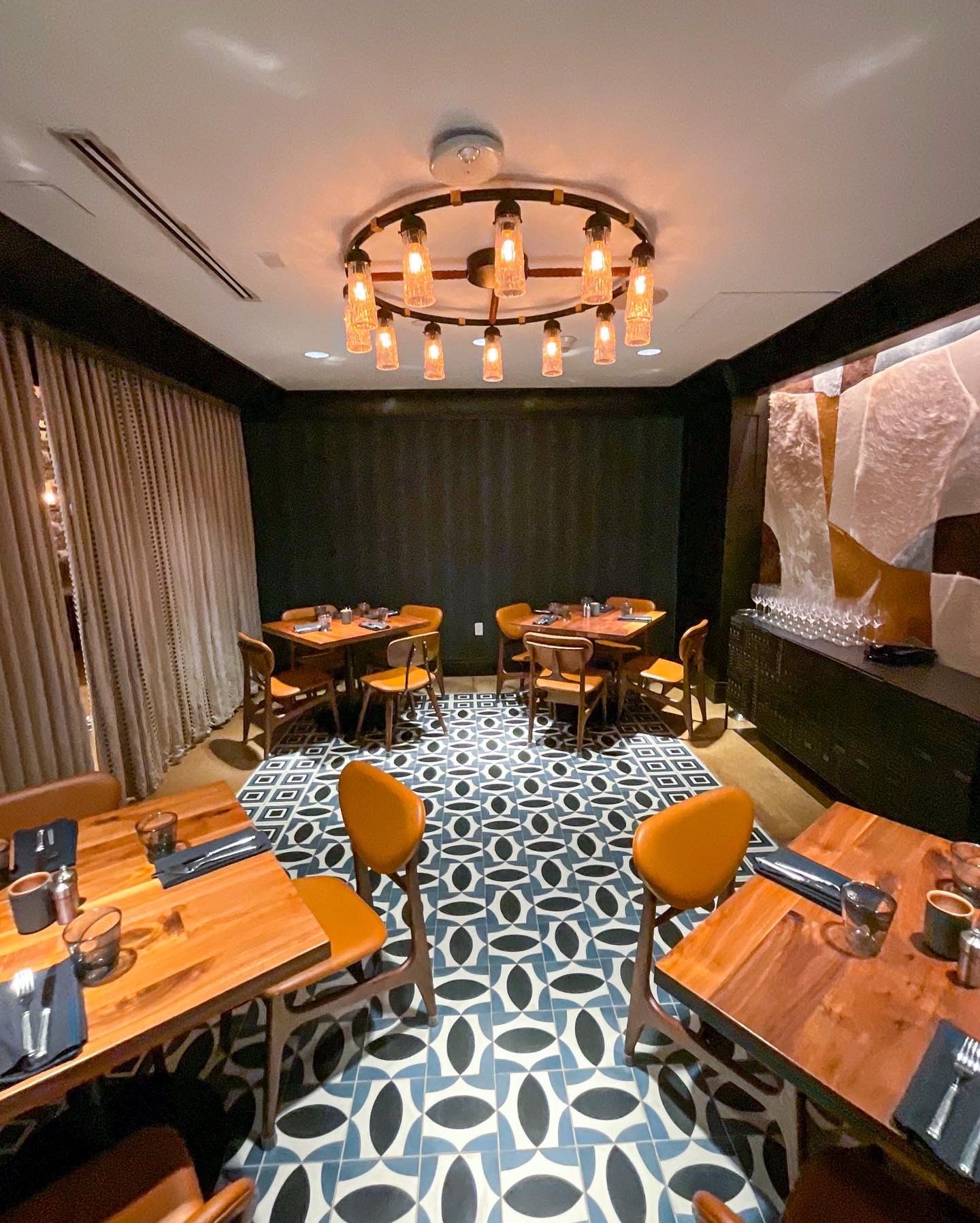 A dining area with wooden tables, yellow chairs, and a large abstract art piece on the wall.